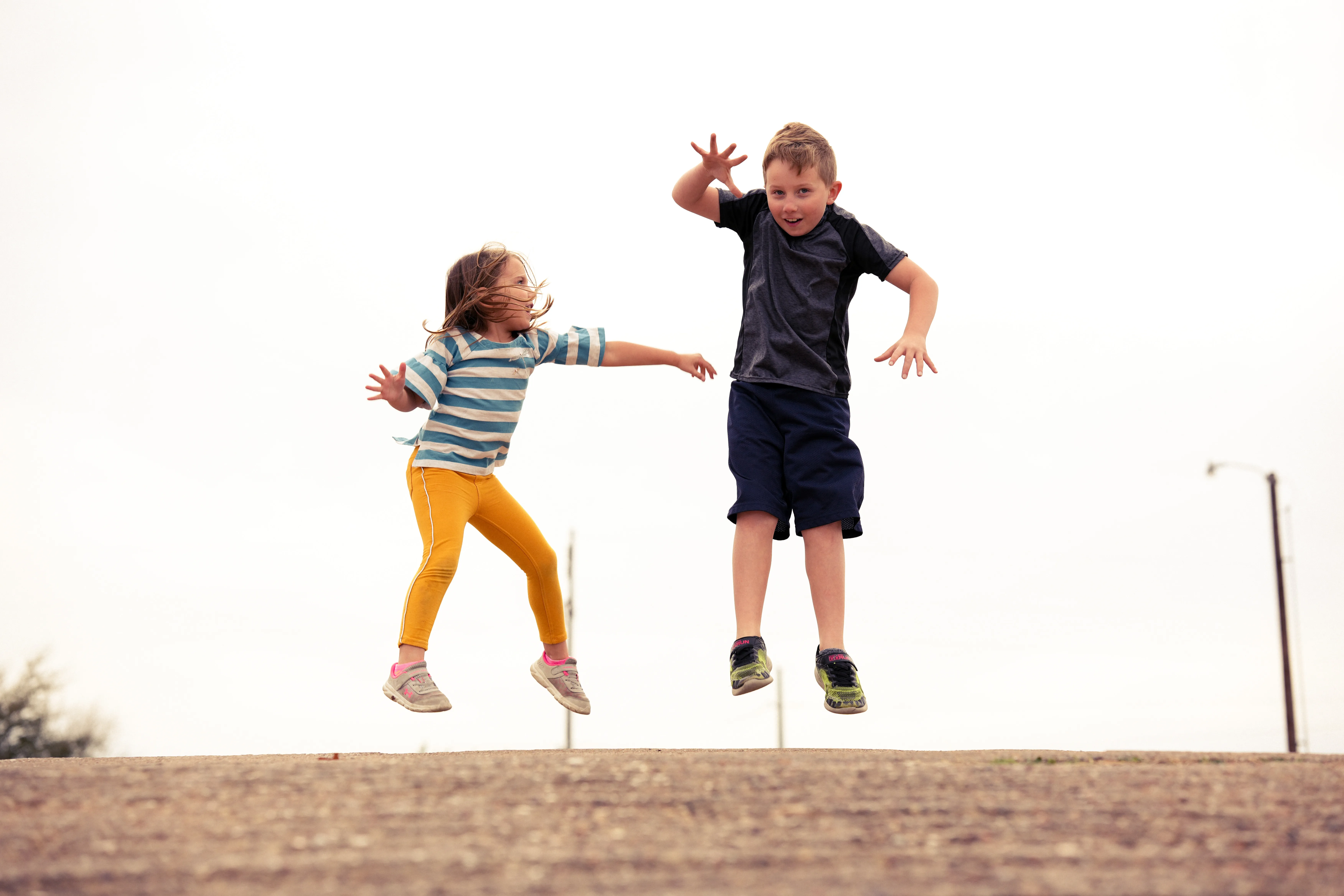 Two children caught mid-jump against a blown-out white sky