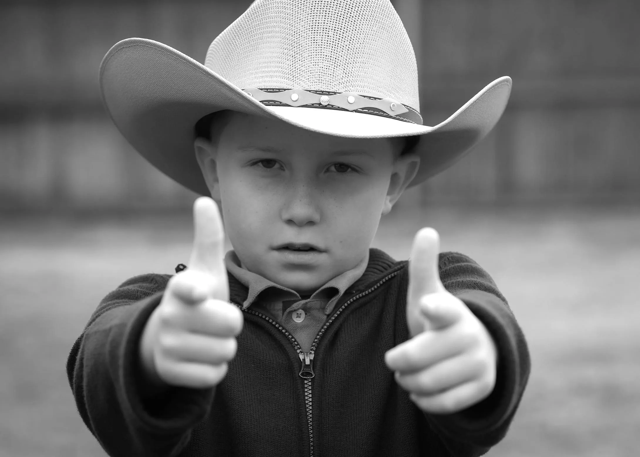 A boy in a straw cowboy hat, both index fingers pointed at the lens
