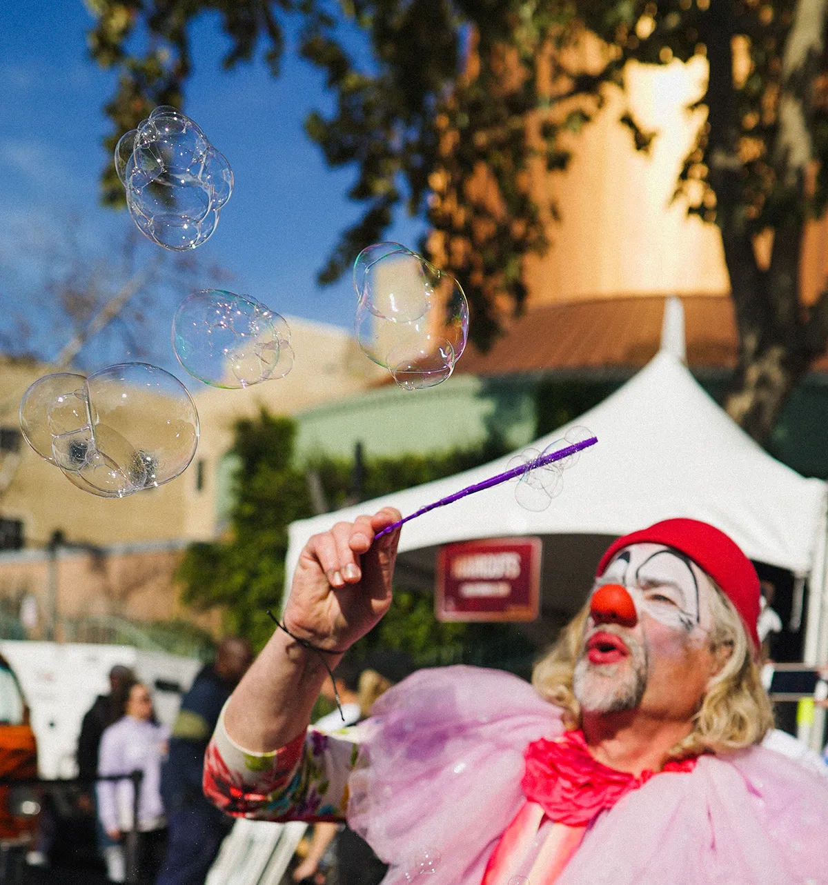 A clown in pink blowing soap bubbles into a blue sky