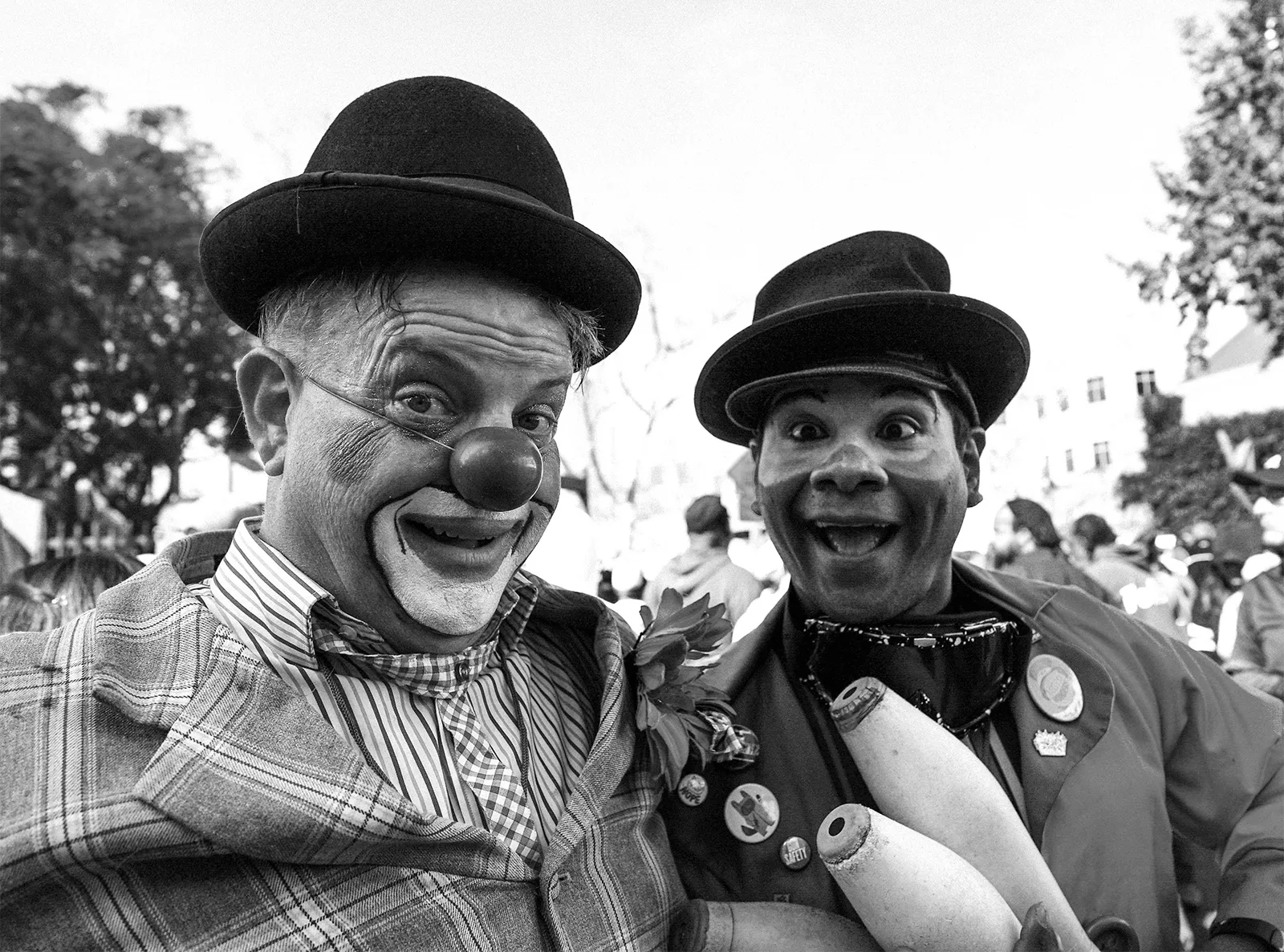 Two clowns in bowler hats leaning into the lens at a street fair