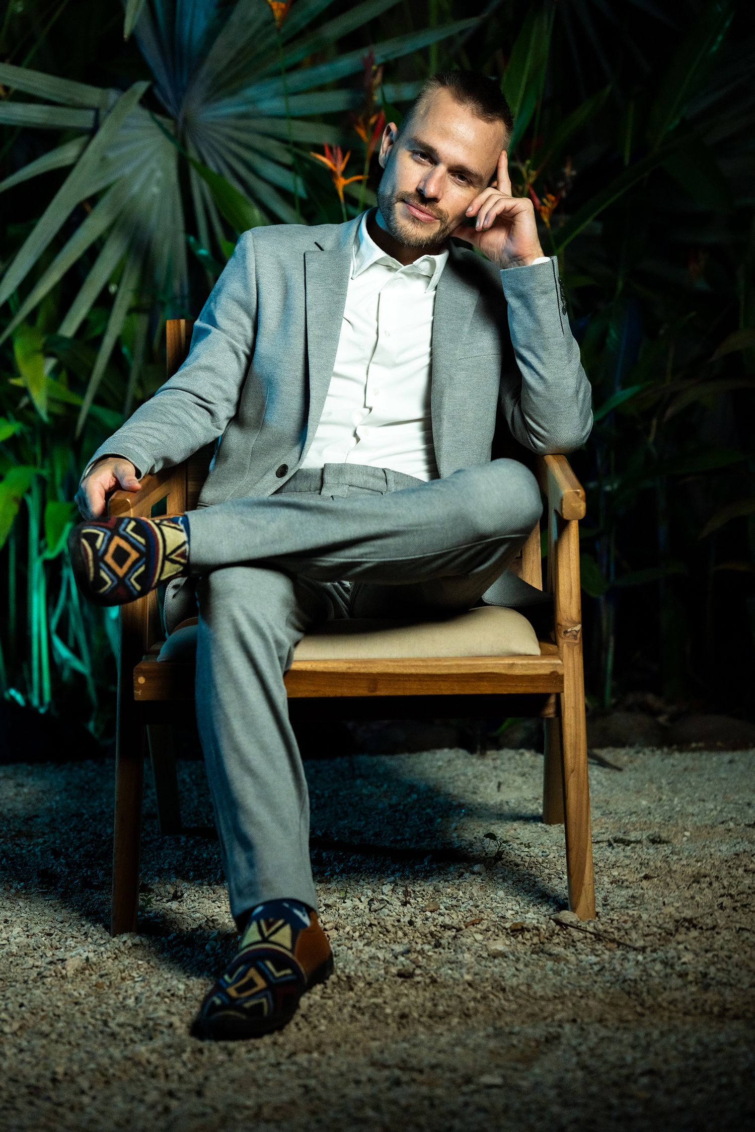 Steffen in a grey suit, seated in a wooden chair before night-lit palms