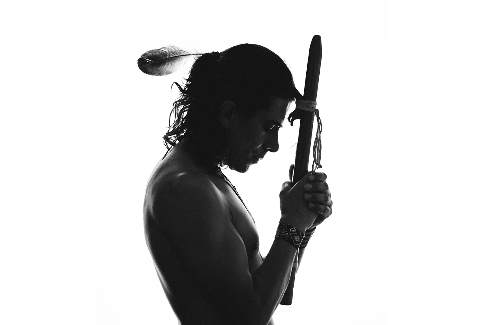 A man in profile against white, a wooden flute held to his forehead