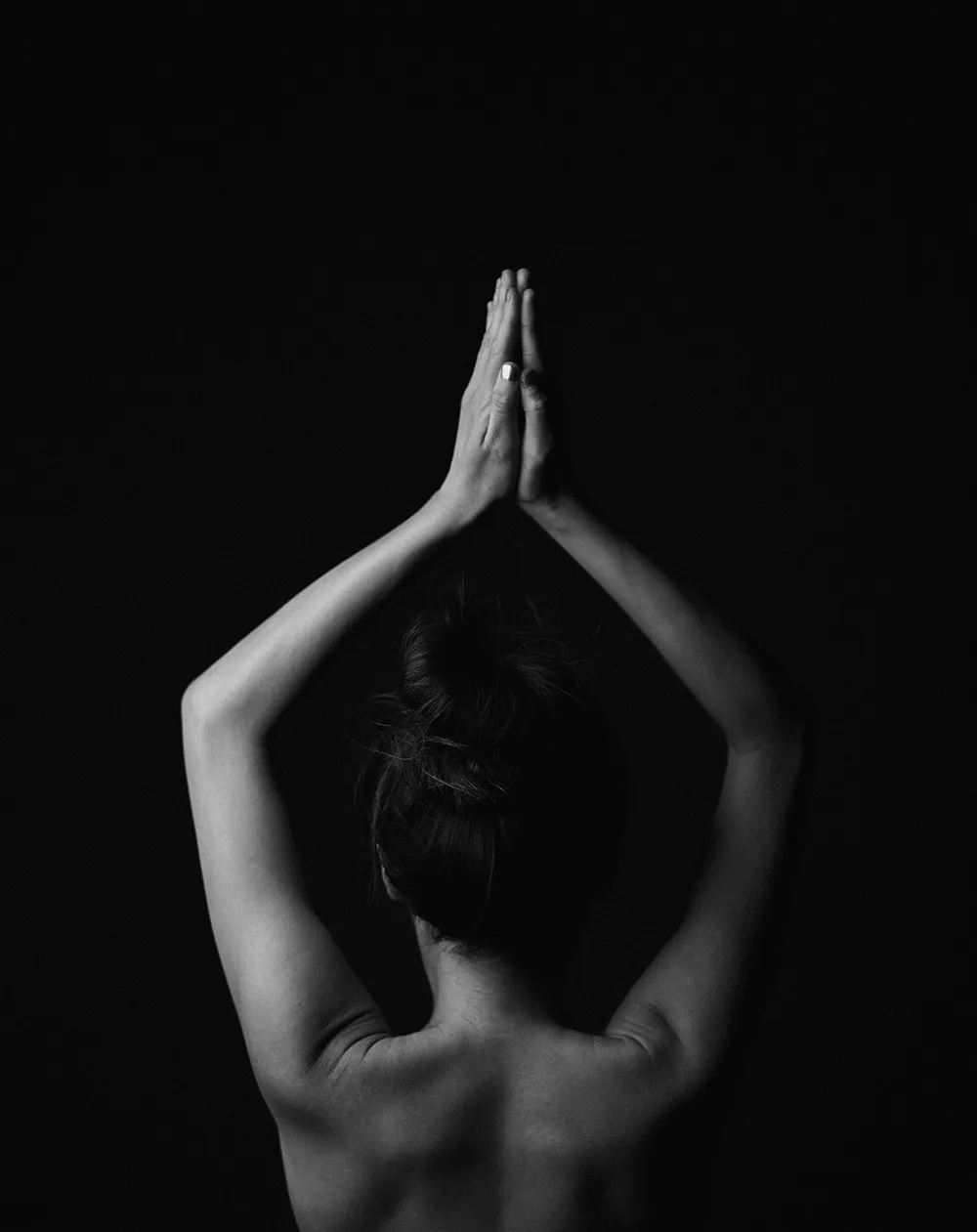 A woman's back in low light, hands pressed together overhead