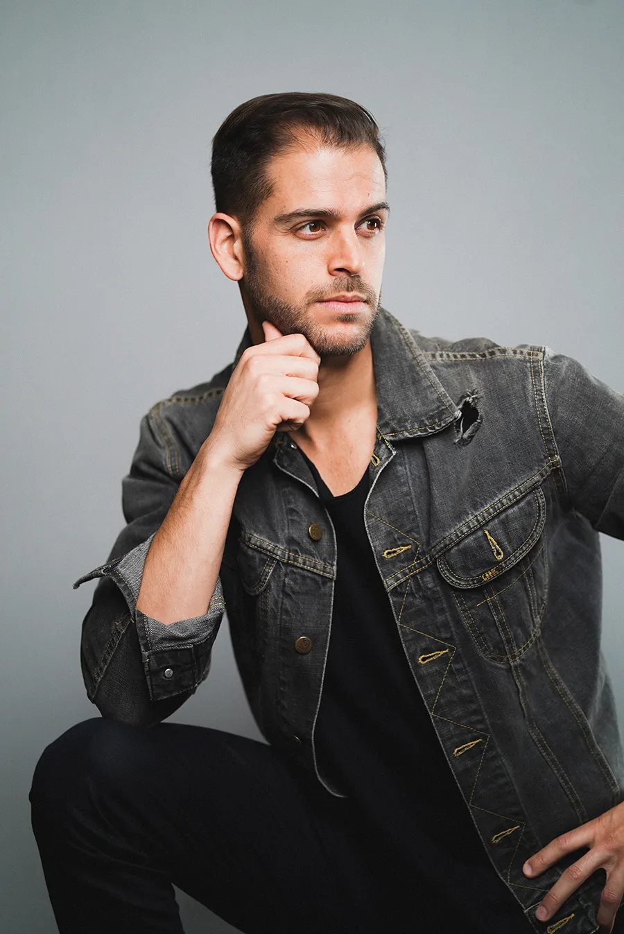 A man in a worn denim jacket, hand resting at his chin